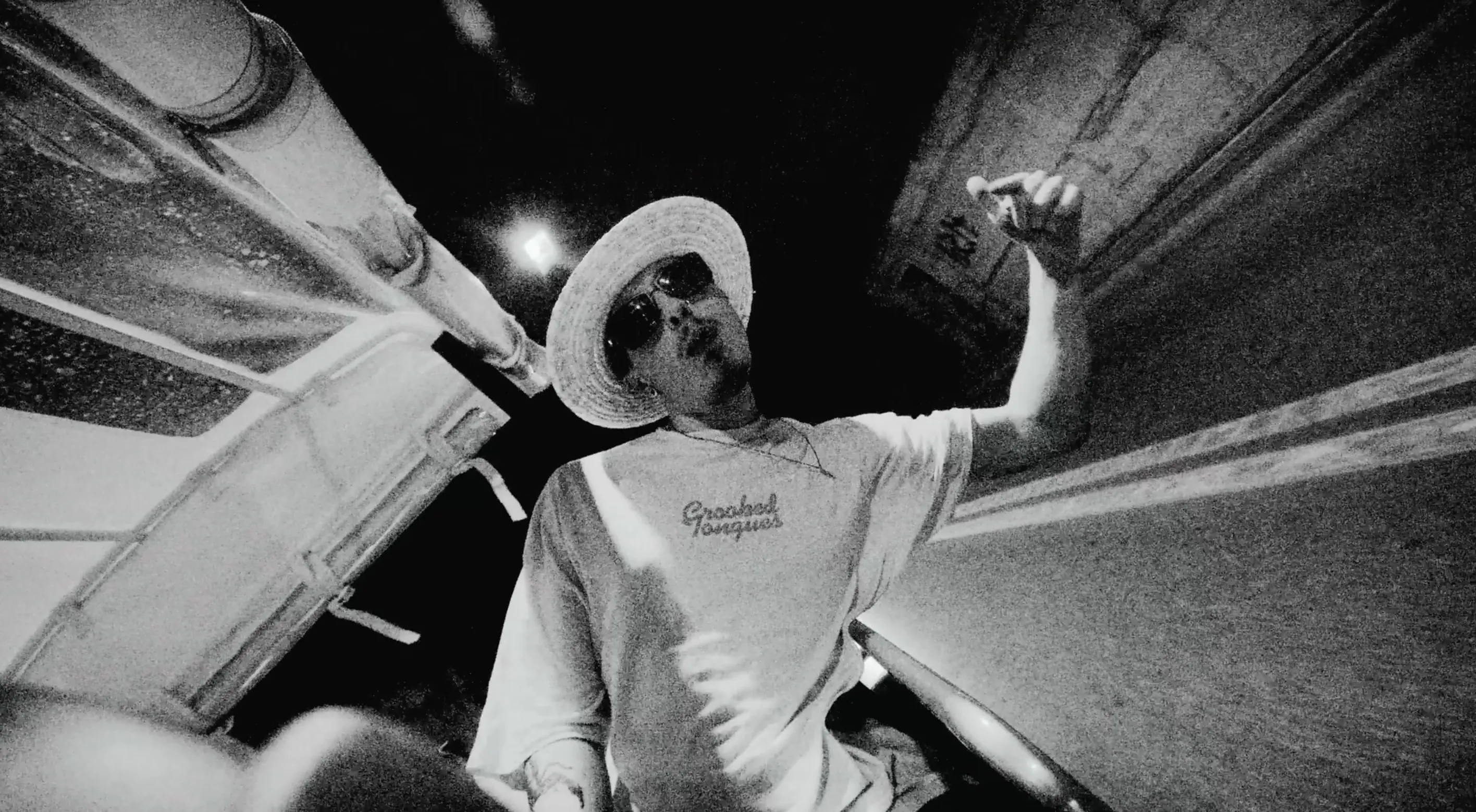 A black and white image of a man posing out of a car
