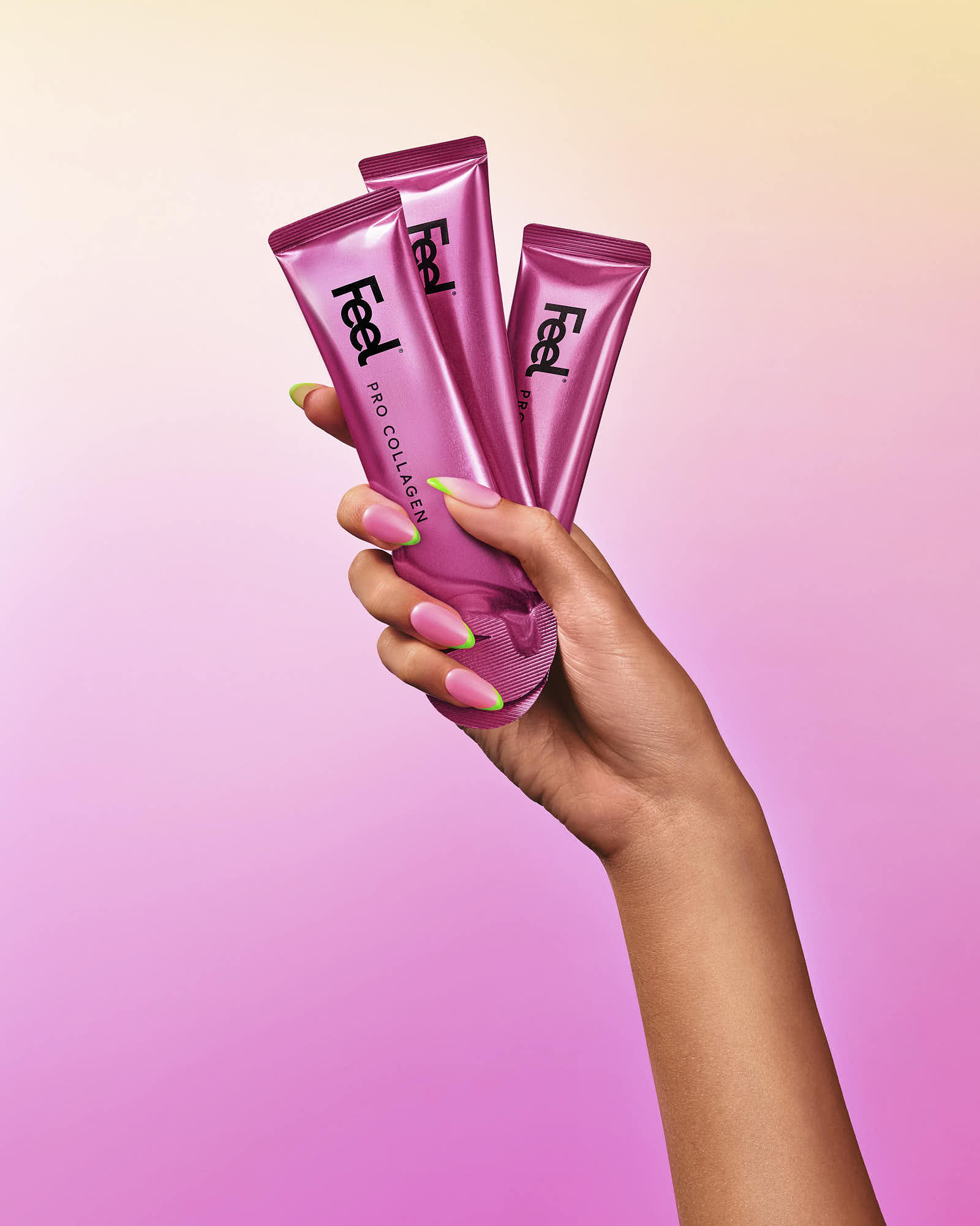 A hand holding three pink tubes against a gradient pink background.