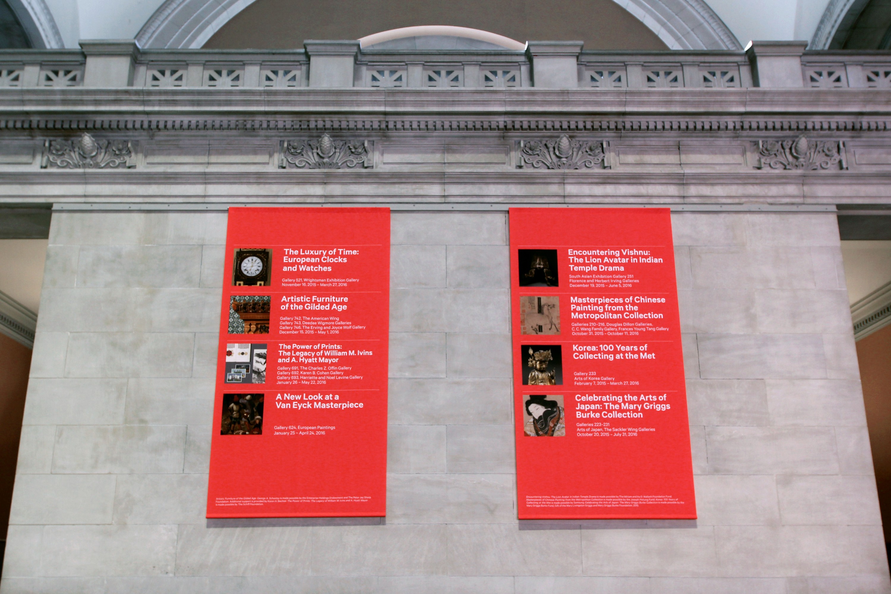 Interior of The Metropolitan Museum of Art in New York showing large red exhibition panels mounted against classical stone architecture.