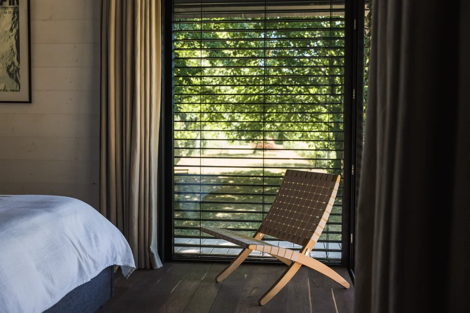 Chambre du Teshima Bourgogne, fauteuil tressé devant la baie vitrée avec stores à lames