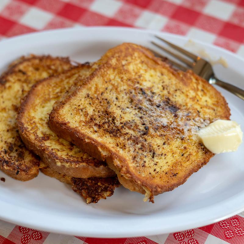 Thick slices of French toast dusted golden brown on a plate with a pat of butter and a fork waiting