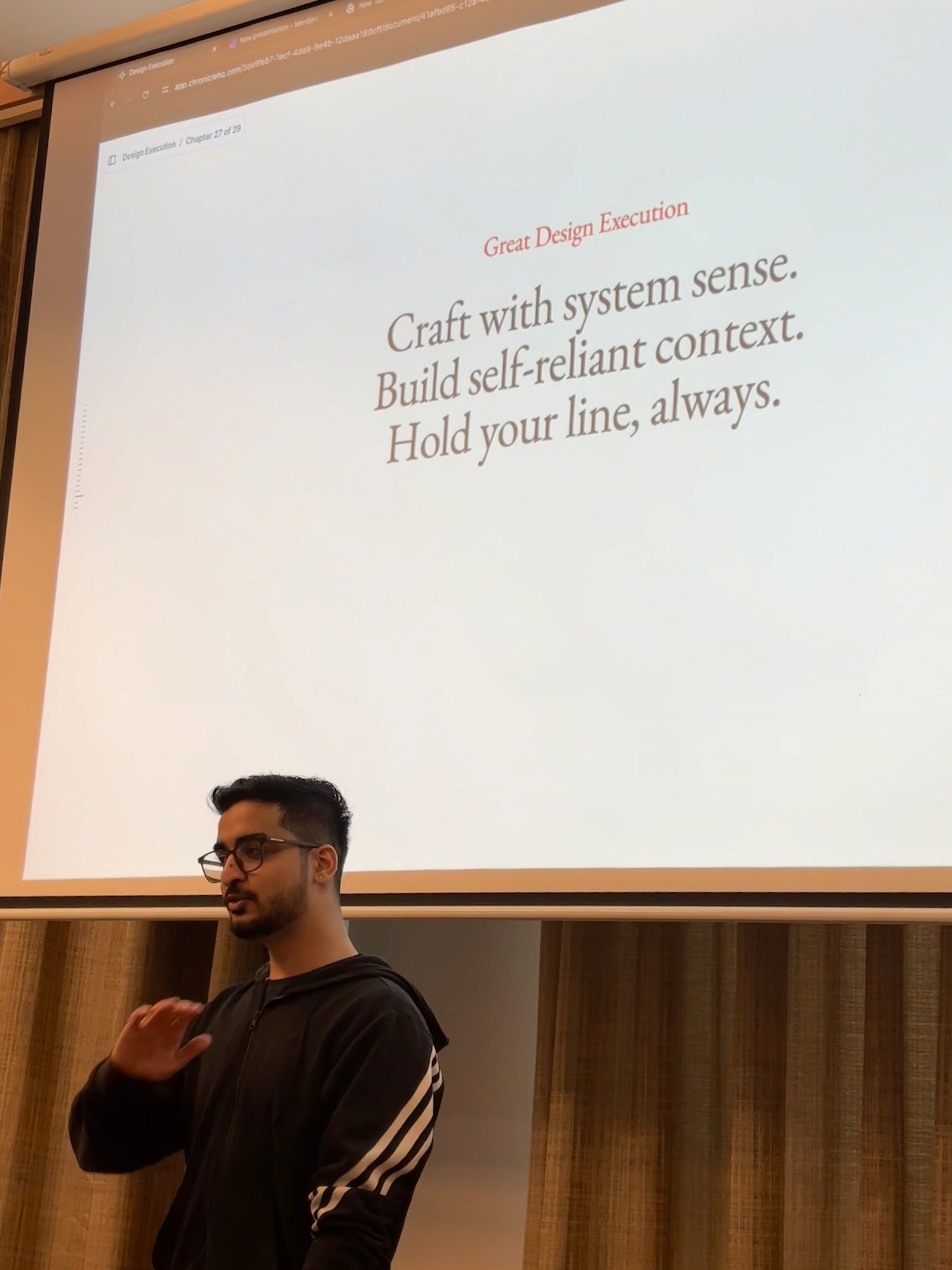 Una persona con una camiseta negra y pantalones de color claro está de pie en la cima rocosa de una montaña al atardecer, sosteniendo una cámara frente a su cara para tomar una foto. Un mar de nubes se extiende detrás de ellos, iluminado por la luz dorada del sol poniente.