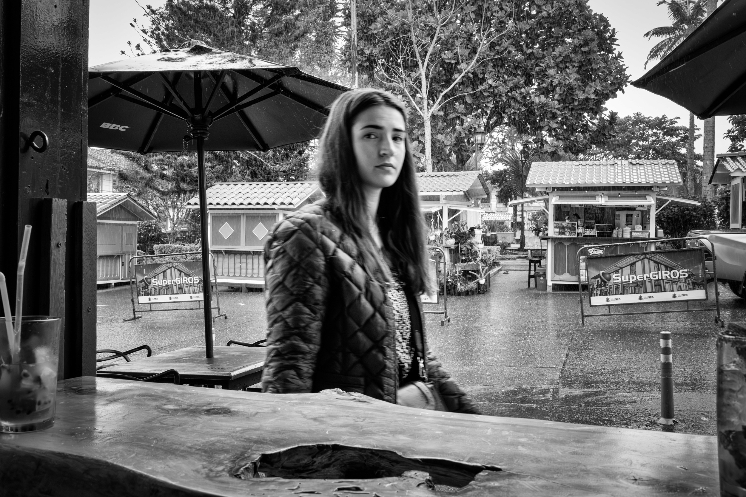 Rainy street scene with people passing by a bar window.