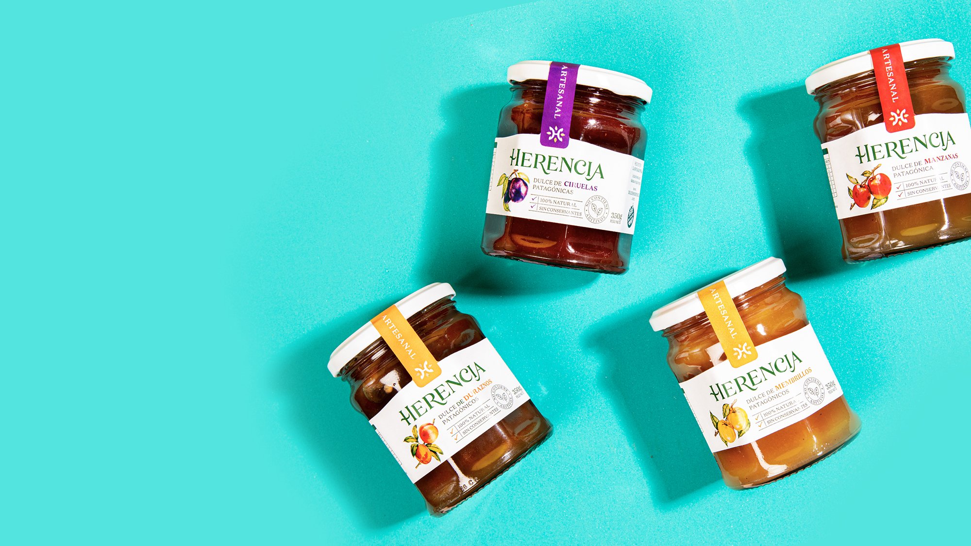 Four jars of Herencia jam with colorful fruit labels are arranged on a turquoise background, evoking a bright and fresh feeling.