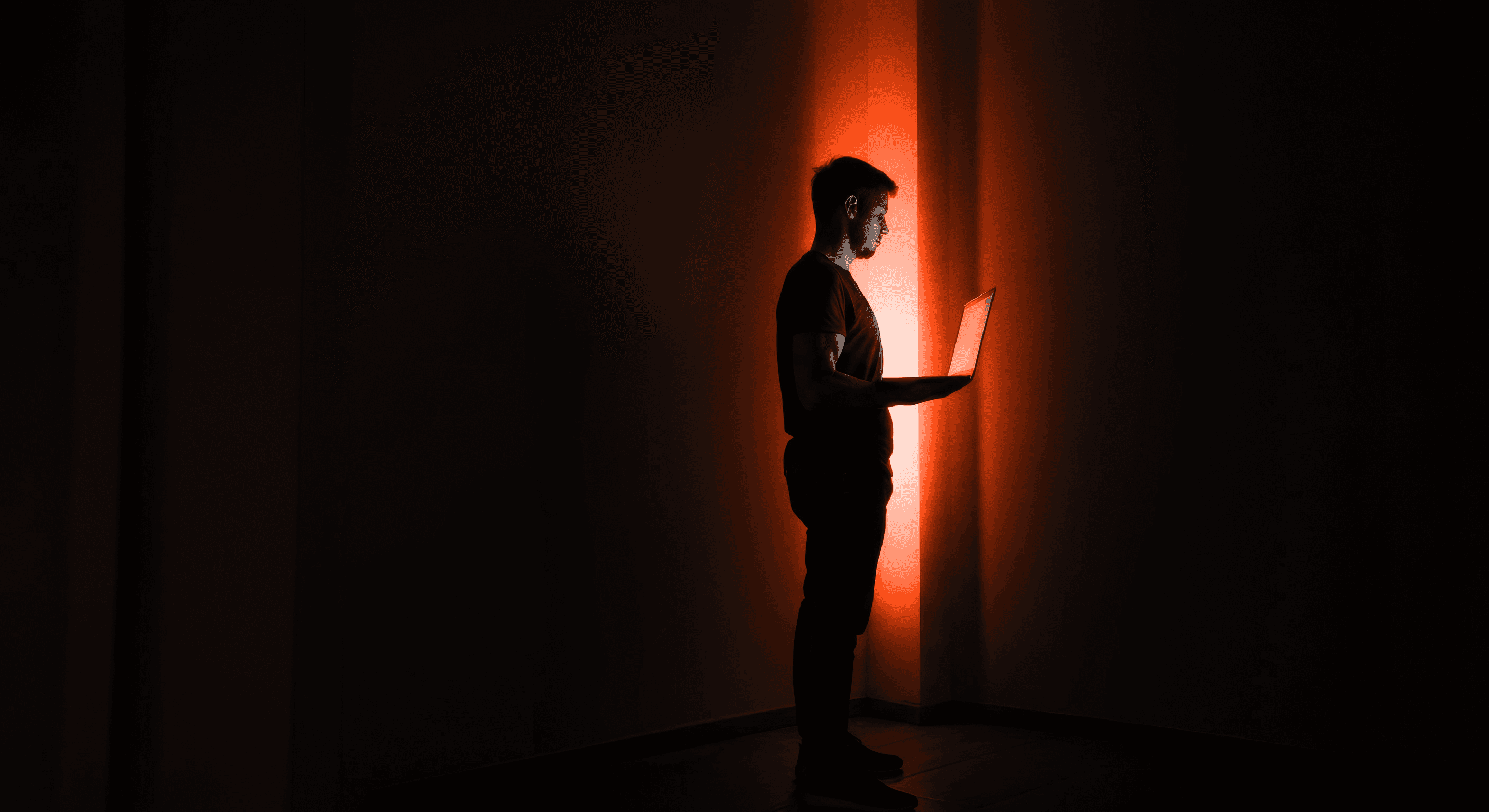 A silhouette of a person standing in a dark space, illuminated by a glowing orange light in the background.