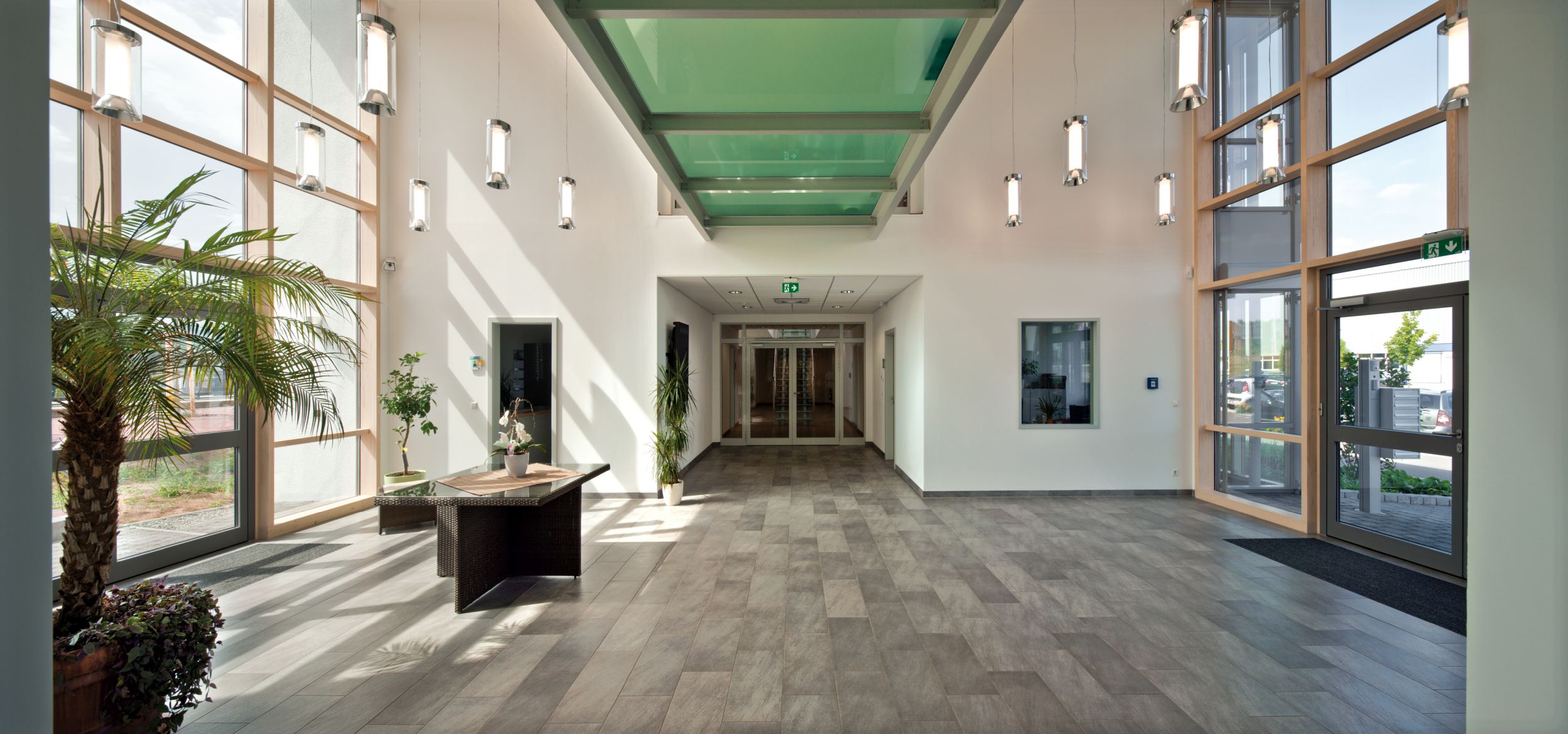 Helles Eingangsfoyer mit großzügigen Fensterfronten, einem modernen Design-Tisch und einem dekorativen Deckenlicht.