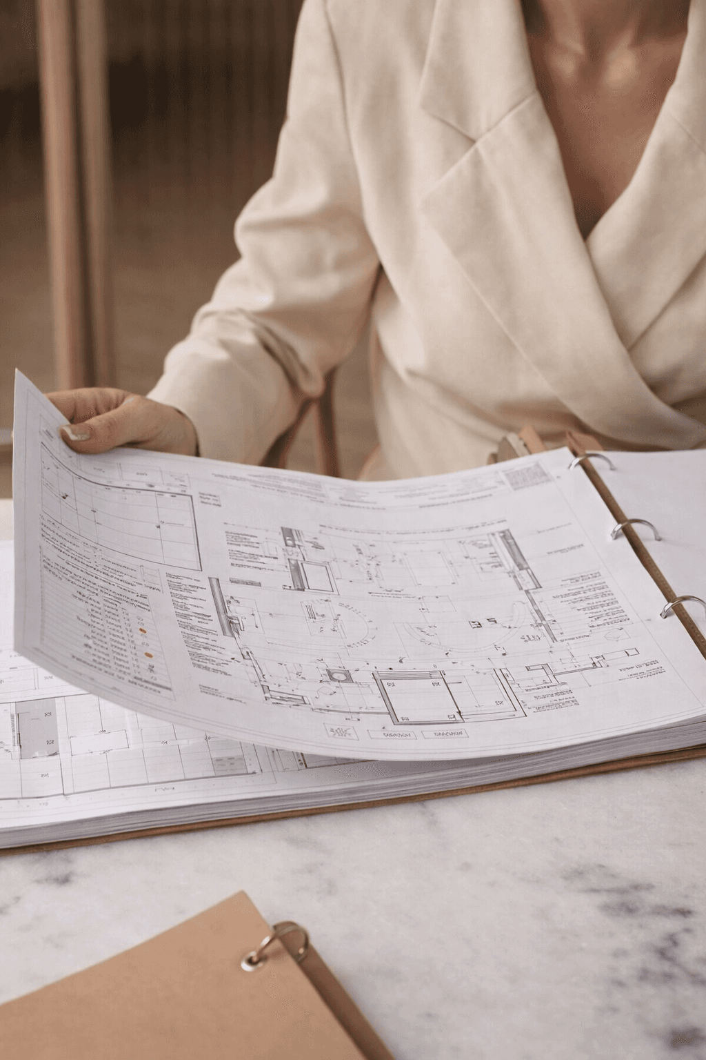 Architecte d'intérieur consultant un plan technique détaillé dans un classeur – préparation du dossier de consultation des entreprises à Bordeaux