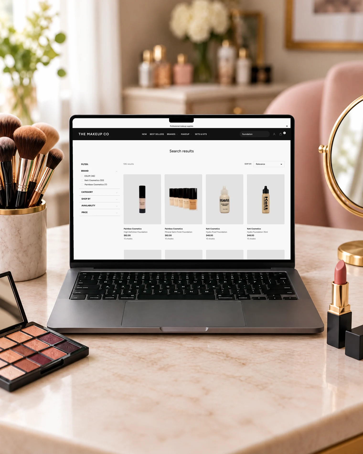 A MacBook on a marble vanity showing search results for foundation on The Makeup Co's store.