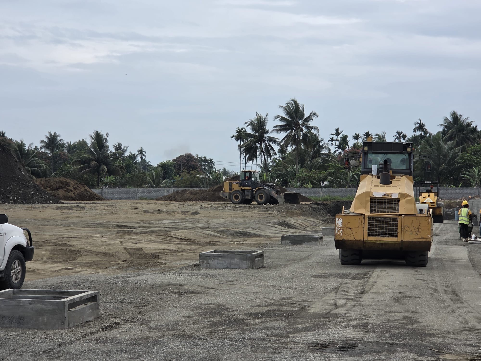 Roller compacting the haul road while crews place blockwork on the boundary wall