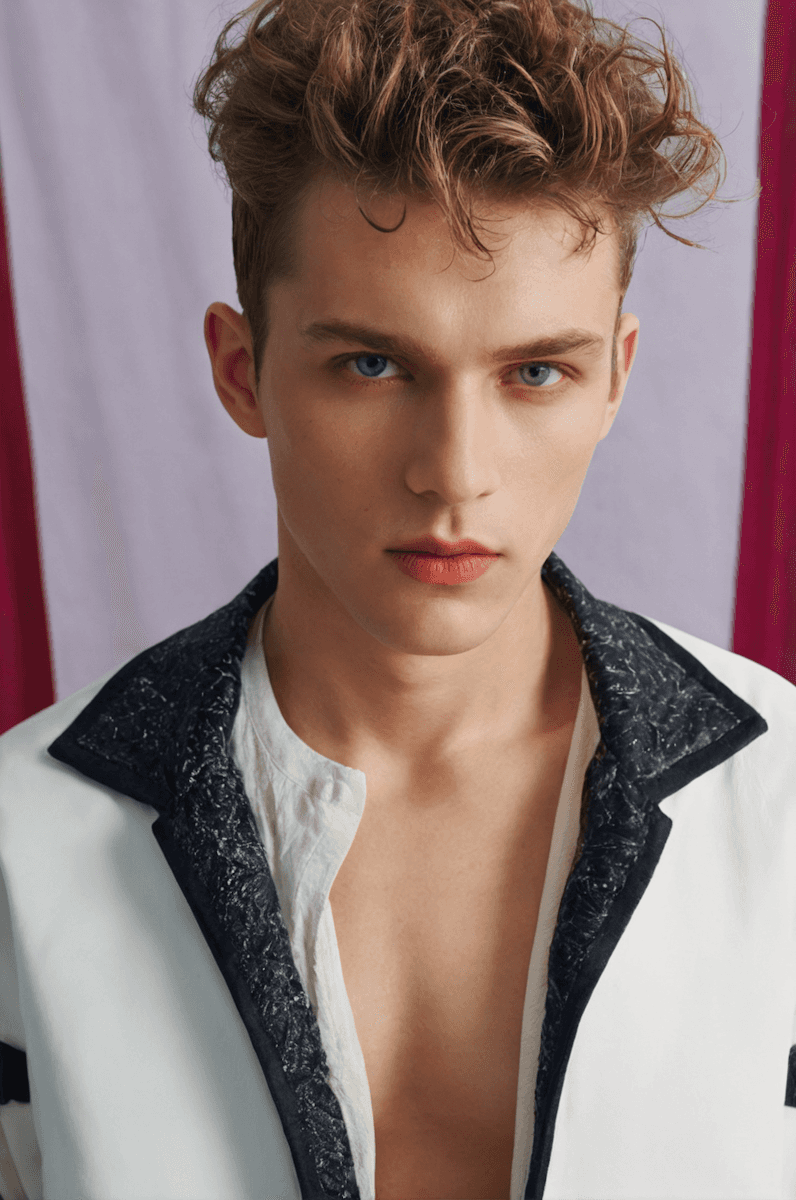 Stylish portrait of a person in a fashionable white jacket with a textured black collar against a softly colored backdrop.