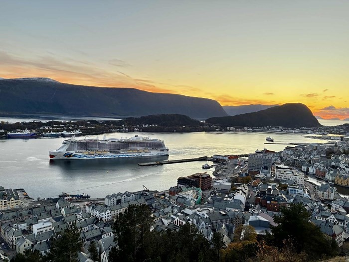 A serene sunset view over a calm harbor with mountains in the background and a boat in the water.