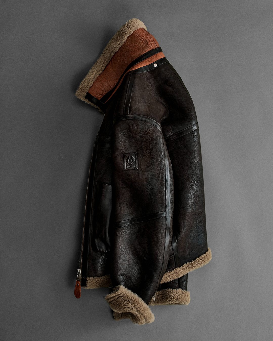 Blouson aviateur en cuir et peau lainé, accroché à un mur gris
