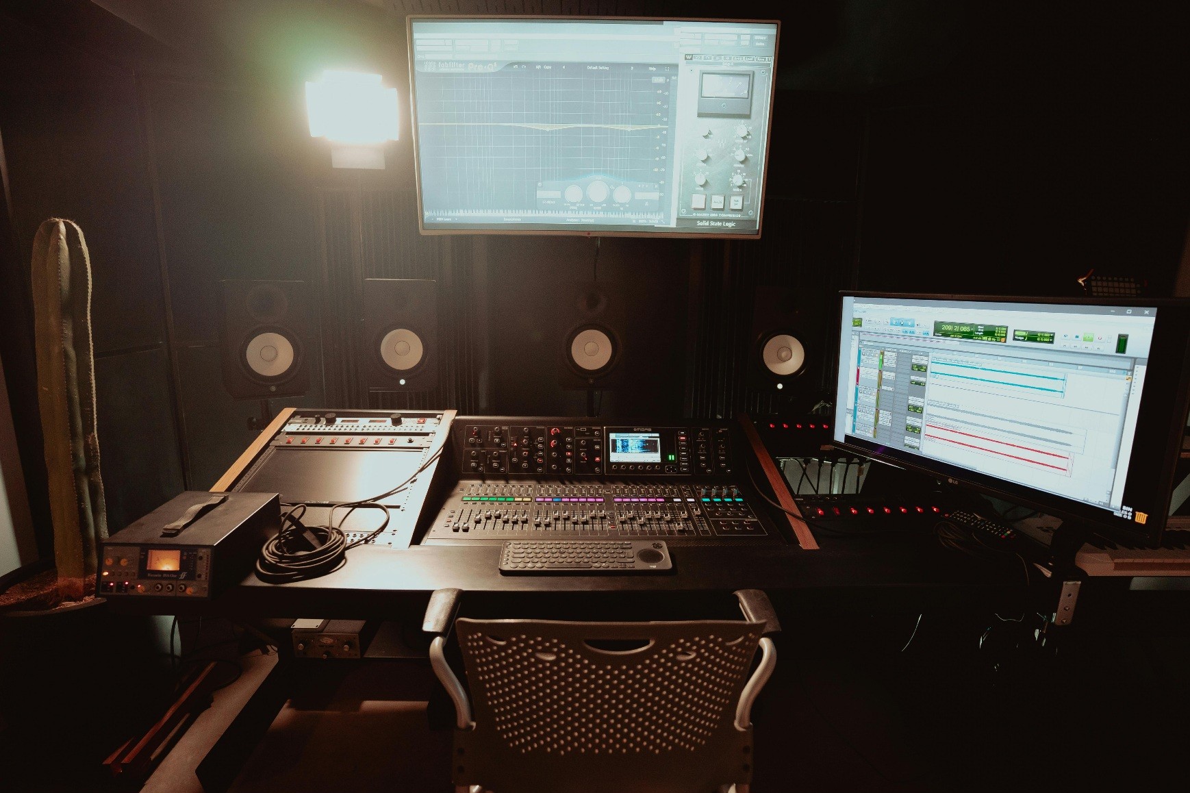 A podcast production company studio with dual monitors displaying sound editing software, a mixing console, and high-quality speakers in a dimly lit setting