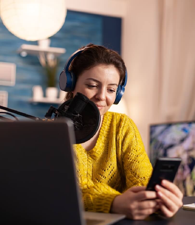 Woman in a yellow sweater wearing headphones, working on a laptop in a focused setting.