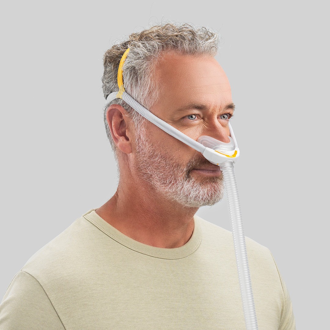 A grey haired man wearing a nasal CPAP machine