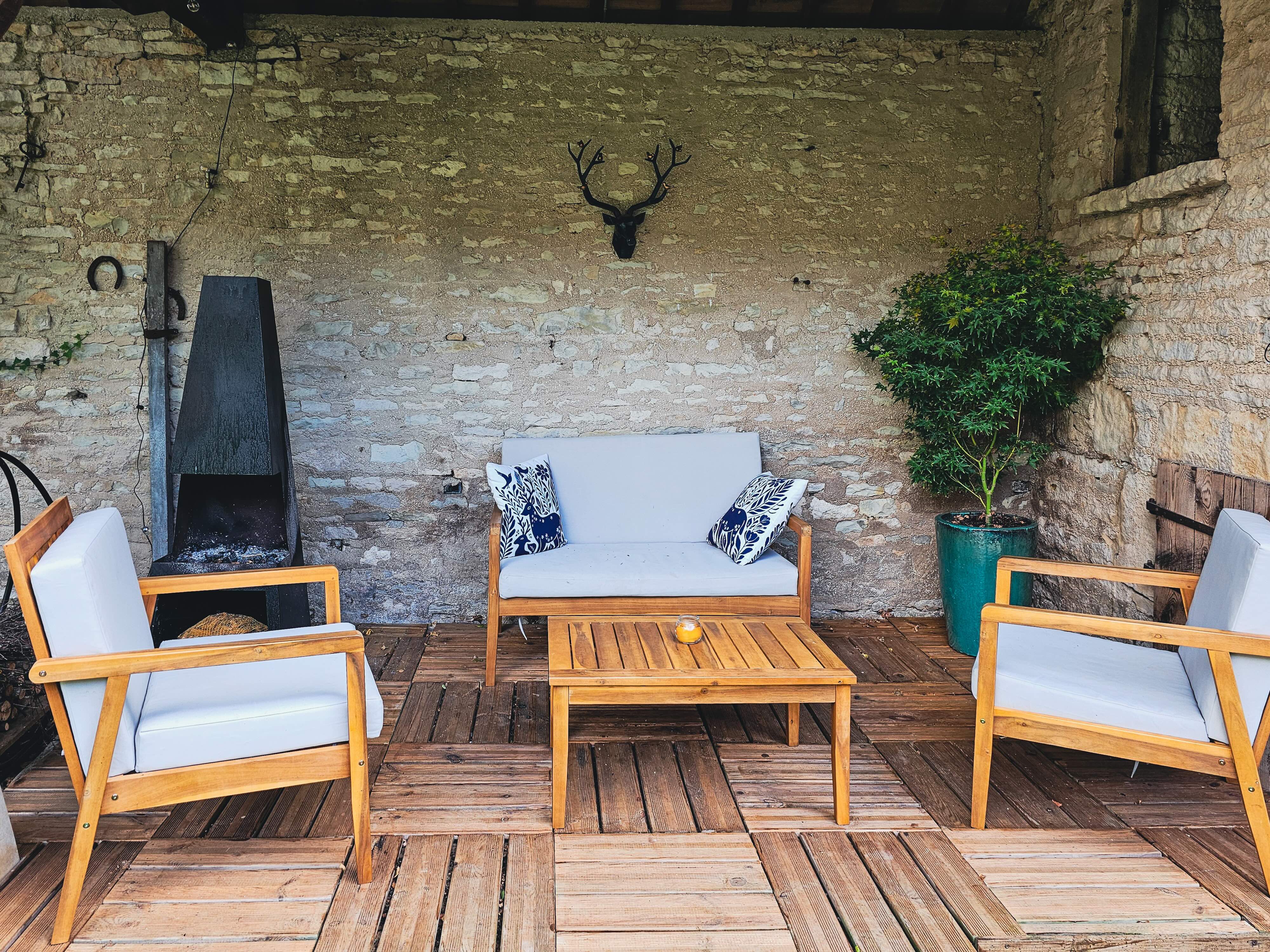 Coin salon extérieur avec fauteuils, canapé, table basse et mur en pierre