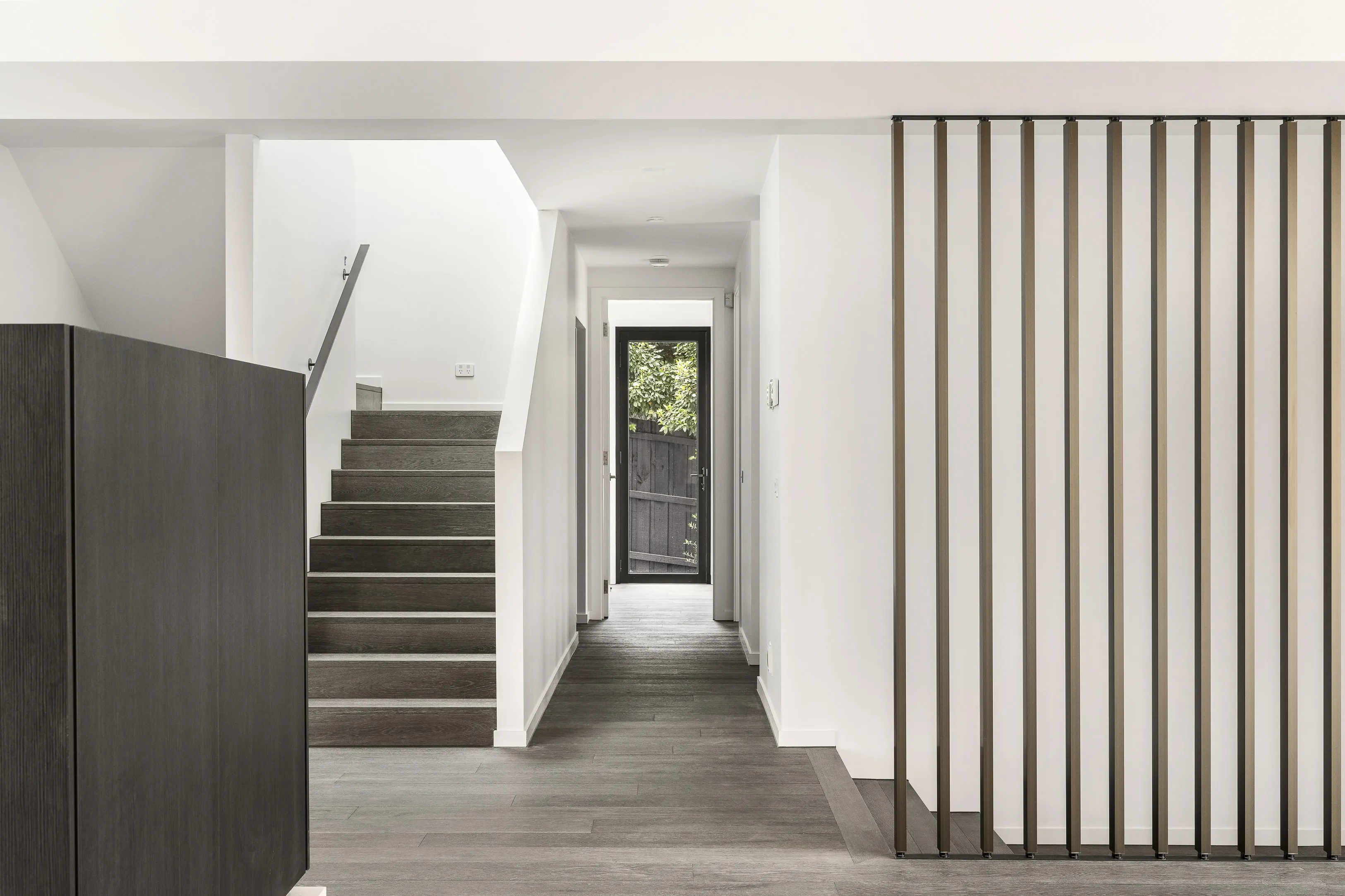 Hallway with a dark timber staircase, charcoal joinery, a bronze vertical batten screen and a glazed door opening to the garden