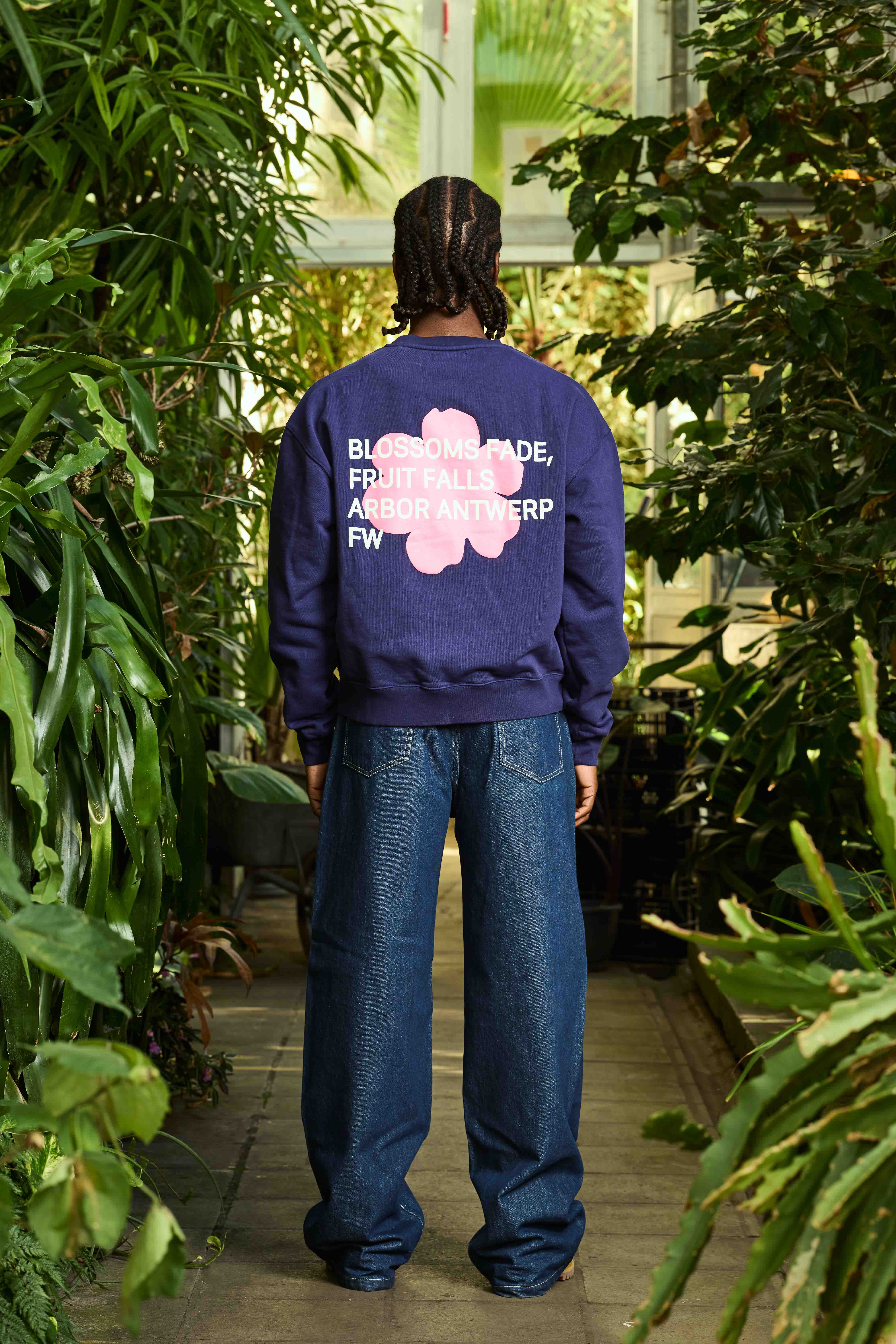 Vu de dos d'un mannequin portant un sweat Arbor Antwerpen imprimé d'une grande fleur avec du texte par-dessus