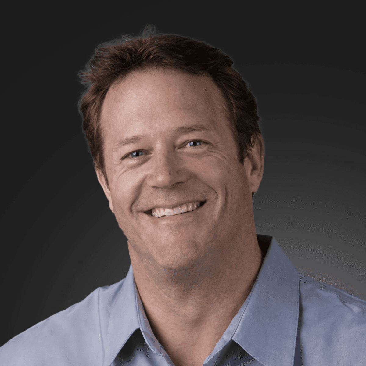 A smiling young woman in a pink blouse stands in an office setting, with soft lighting and a professional backdrop.