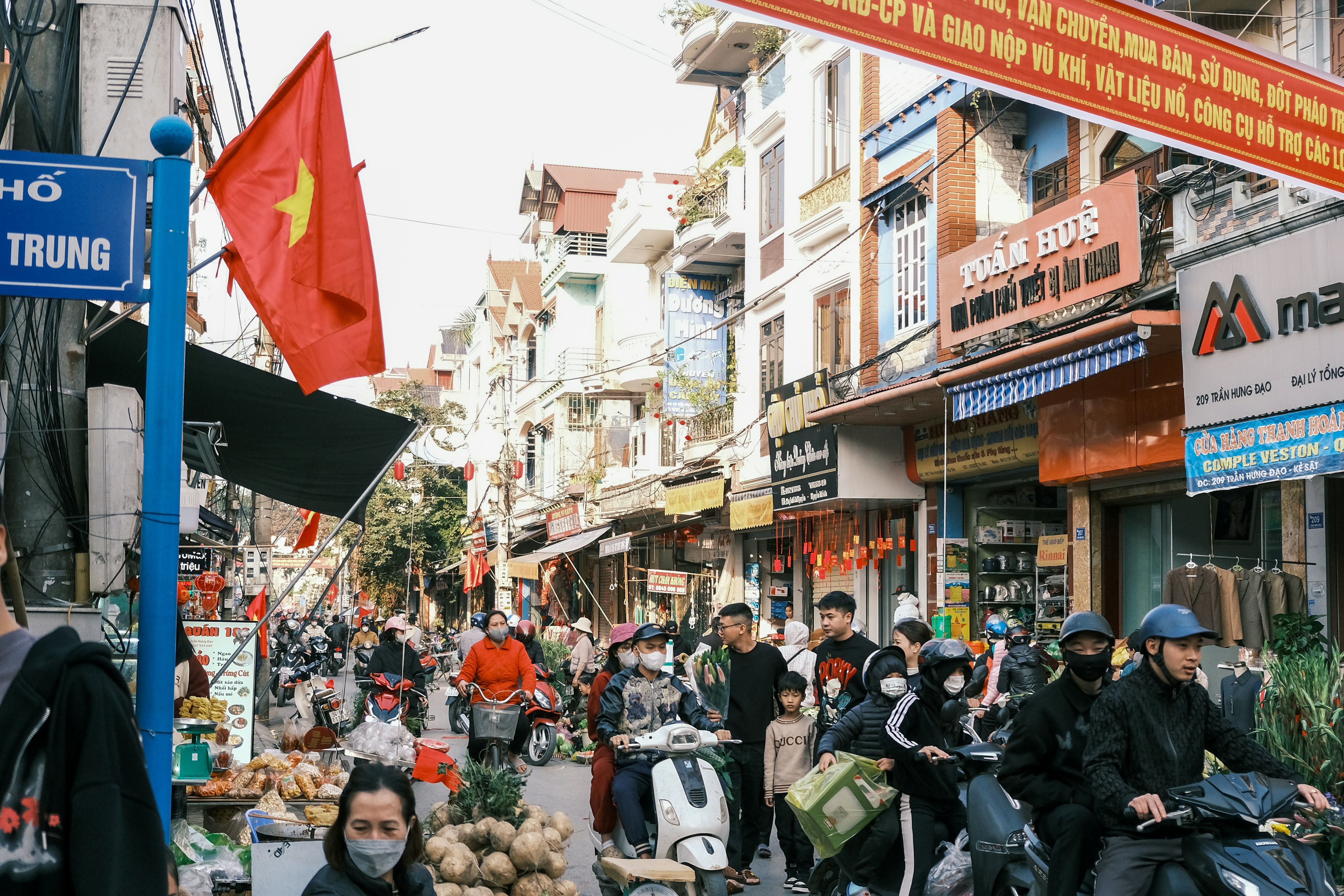 Busy street scene in vietnam, with scooters and flags.