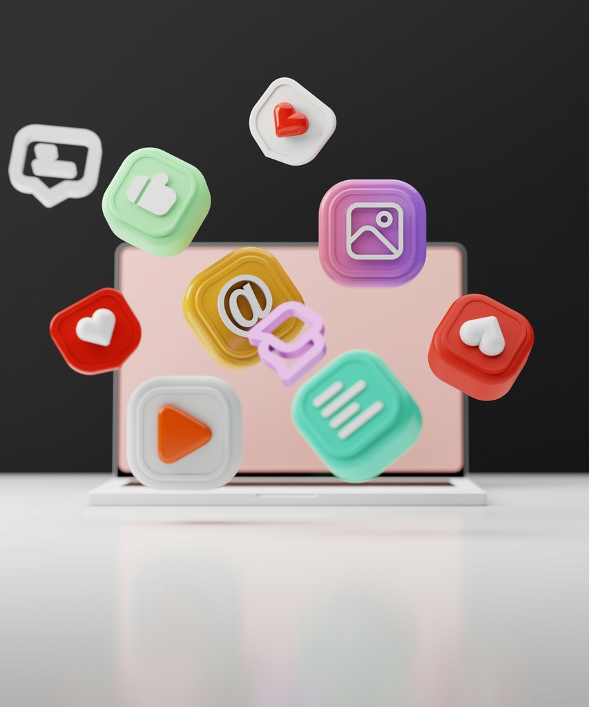 A laptop with a pink screen is surrounded by floating, colorful 3D social media icons, such as likes, messages, and notifications, representing the dynamic nature of digital interactions and online connectivity.