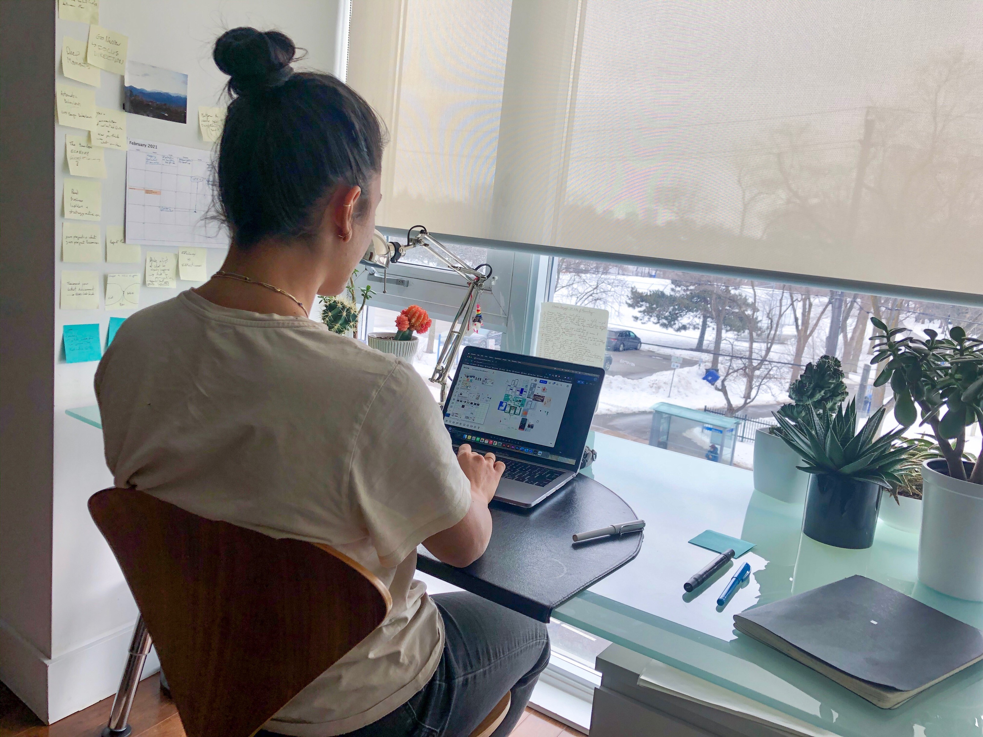Modern home office setup with a monitor, ergonomic chair, keyboard, and indoor plants near a window with blinds.
