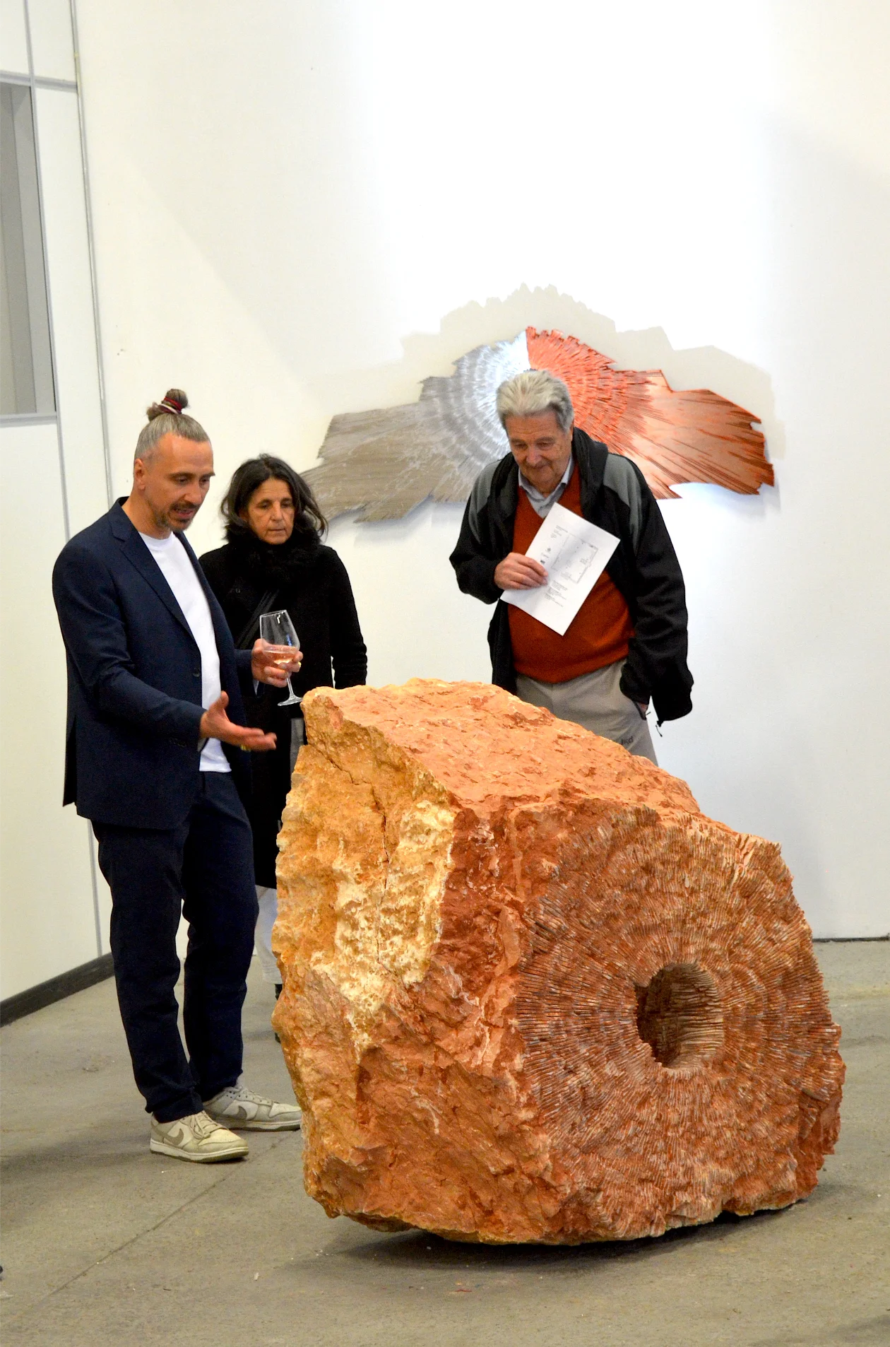 Installazione iStone Arte con blocco di pietra rossa lavorata e opera murale radiale contemporanea, sinergia tra arte materica e design per brand