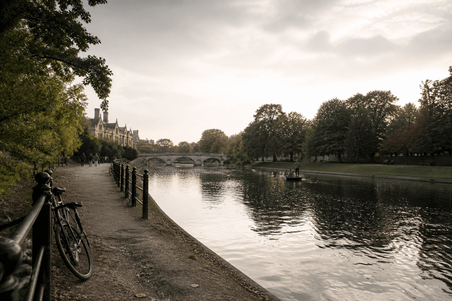 Riverside path along the River Cam in Cambridge during early evening, with bicycles by a railing, a punt on the water, and soft natural light reflecting off the river.