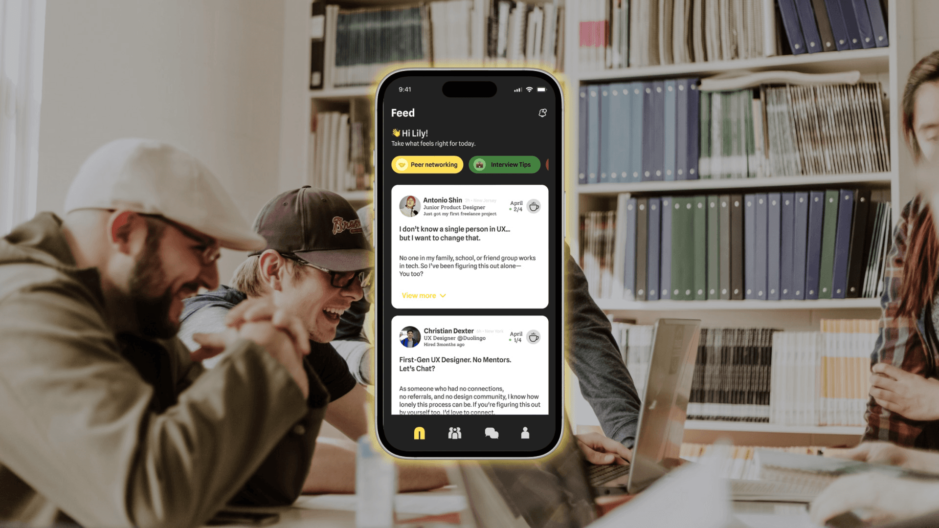 A smartphone displays a Feed interface showing two user profiles: one labeled “Antonio Shin” with a message “I don’t want to change a single person in my family. I’m not going to change that,” and another labeled “Christian Dexter” with a message “First-Gen User Designer As A Chatbot.” The phone’s screen also shows “Feed” at the top and “View more” buttons below. The background is blurred, showing a bookshelf and people seated around a table.
