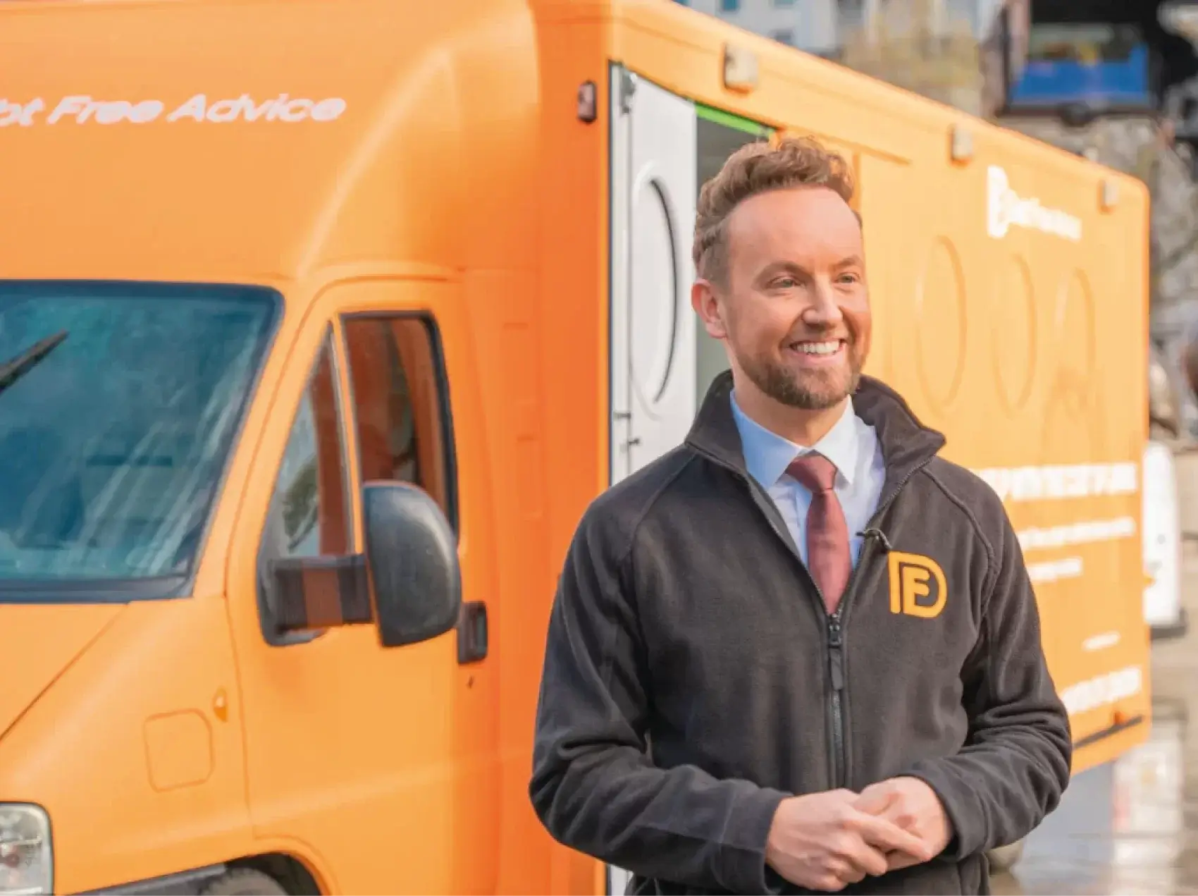 Matt Dronfield stood in front of an orange Debt Free Advice van