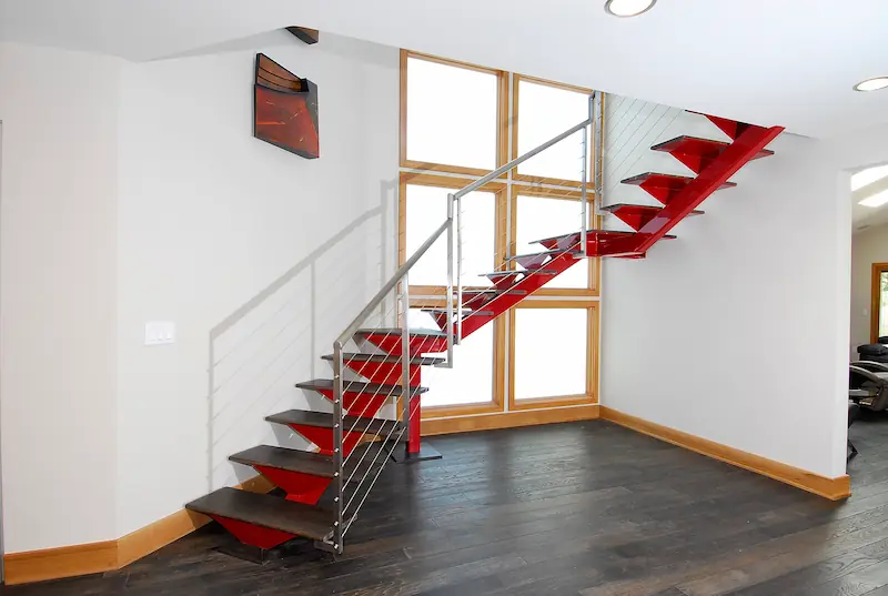 A red, modern steel staircase with stainless steel handrails with cable rails. Large, 6 panel picture window with obscured glass, letting in abundant natural light. Irvine Transitional Modern Project. Photo by Chris Darnall.