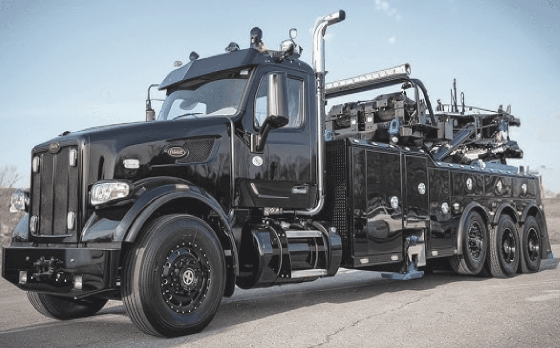 A large black semi truck equipped with a crane, parked on a construction site.