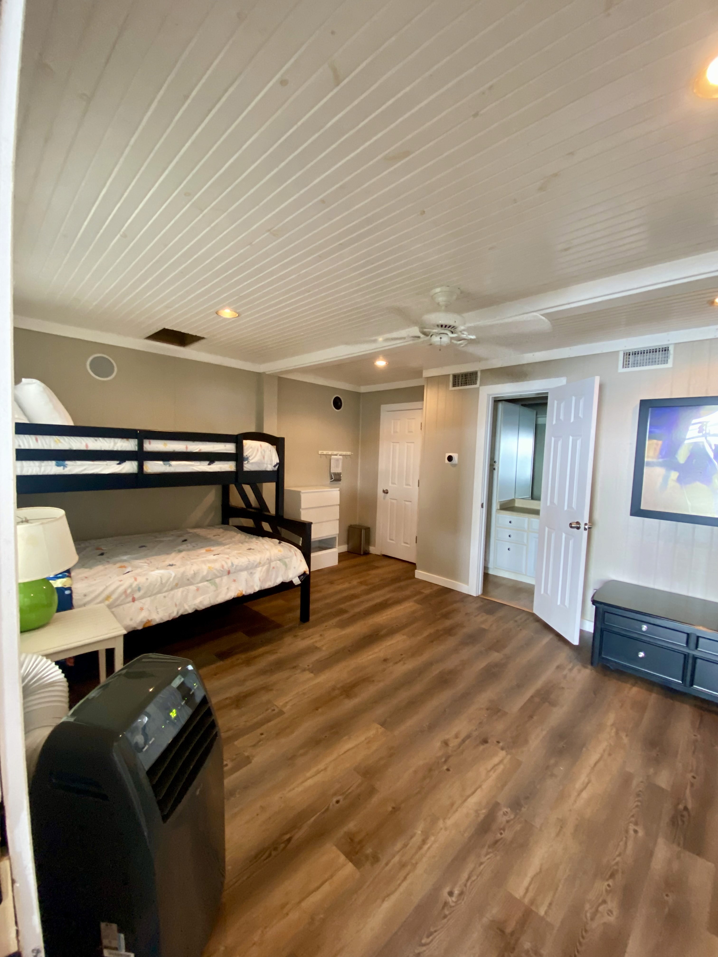 Bedroom interior with bunk beds, an air conditioner, and a door leading to the bathroom. Hardwood flooring.