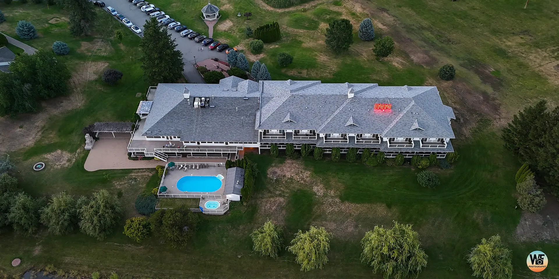 Aerial view of a large building with a swimming pool surrounded by grass and trees.