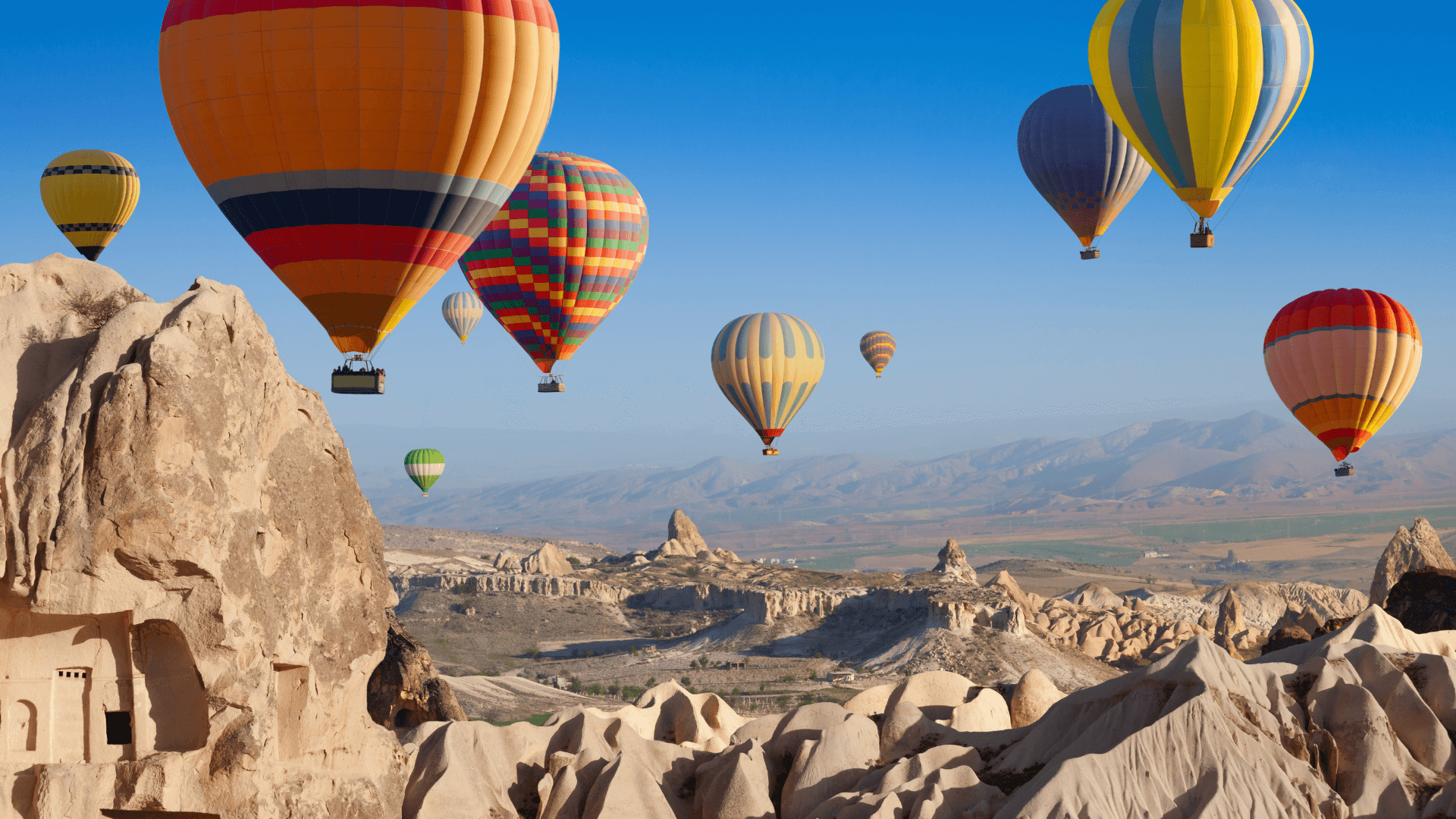 Colorful hot air balloons floating above the fairy chimneys and rock formations of Cappadocia, Türkiye’s iconic travel destination.