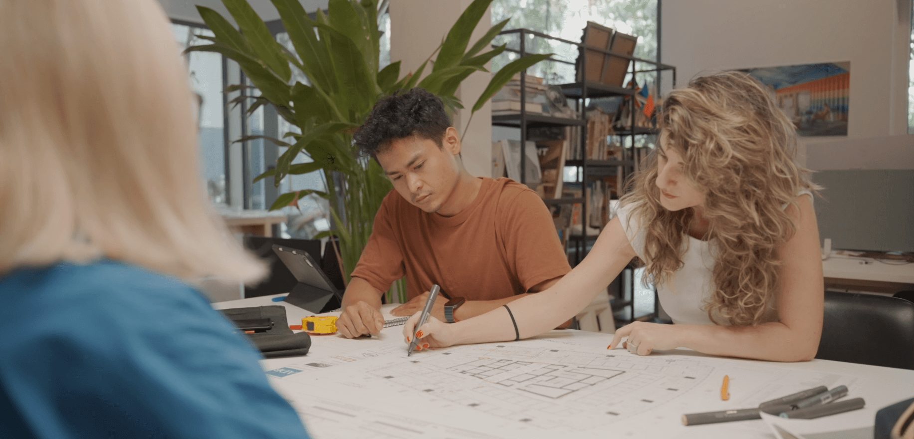 Project stakeholders reviewing technical architectural drawings in an office setting, illustrating the coordination between design documentation and accurate building records for handover