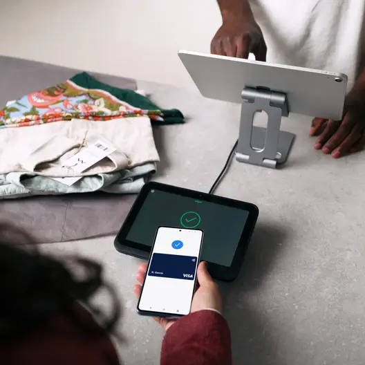 A young person with curly hair smiles at the camera while sitting in front of a laptop against a dark background.