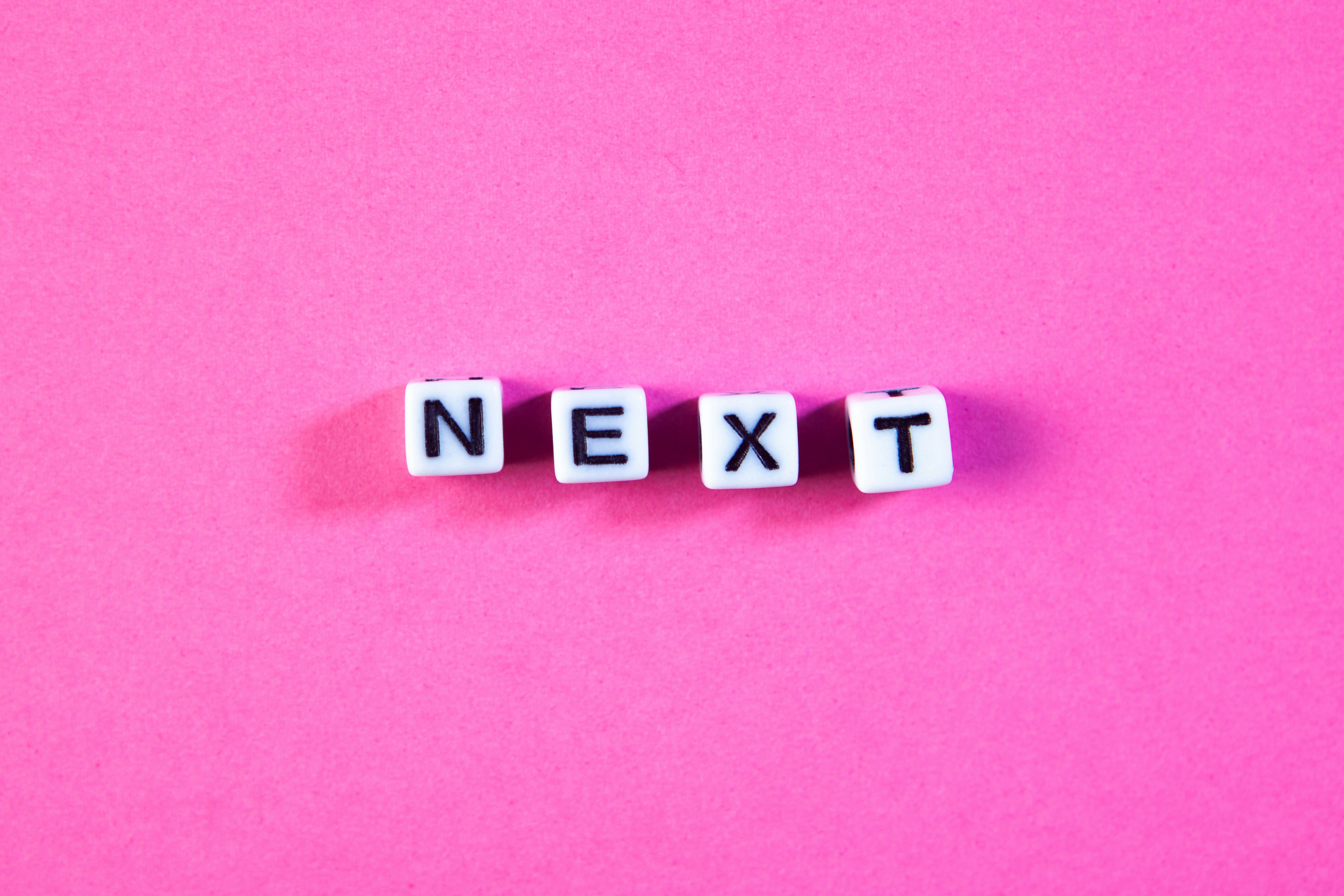 White letter beads spell out next on pink background