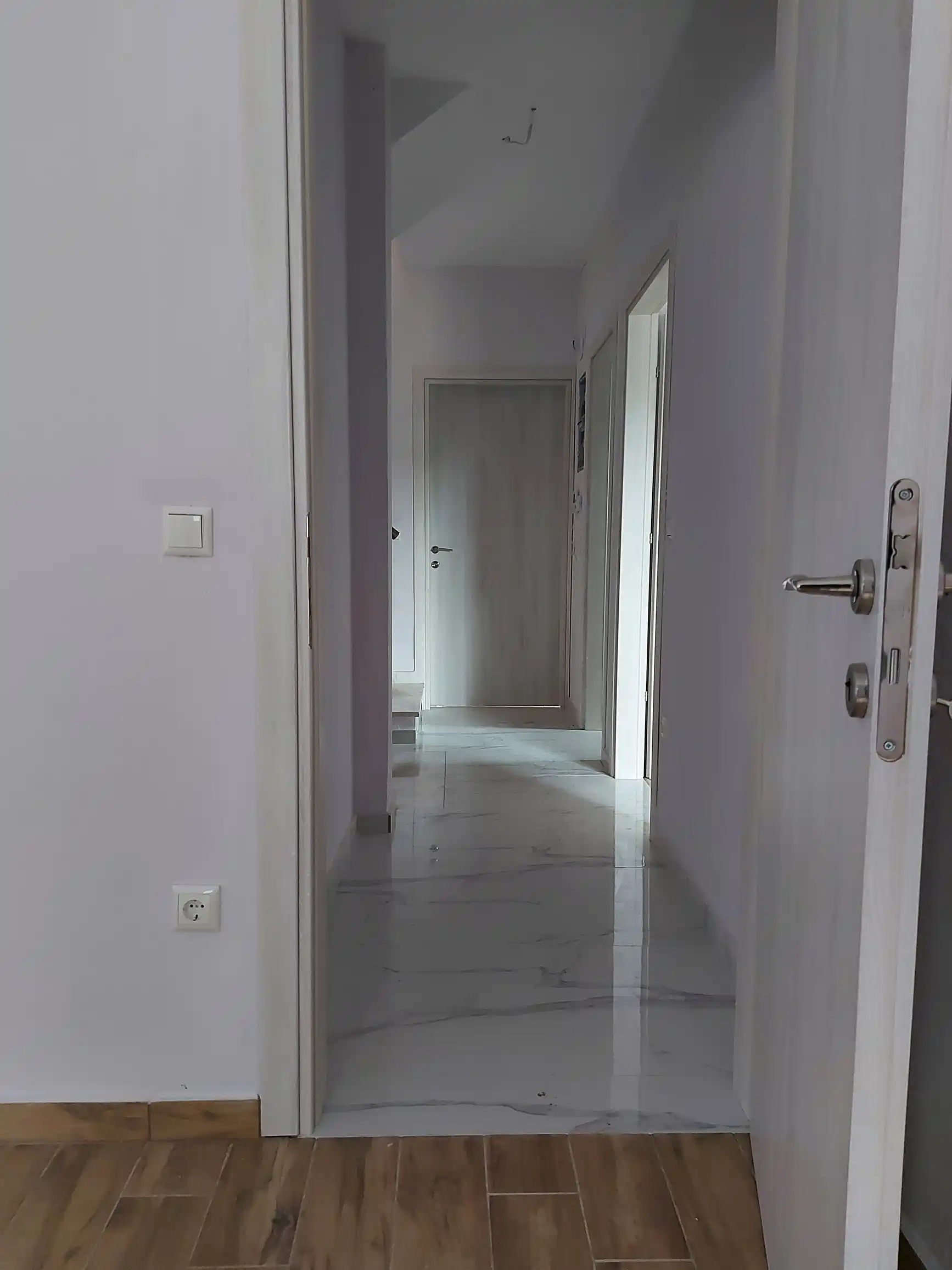 Λυκή ξύλινη πόρτα δωματίου ανοιχτή όπου φαίνεται το χωλ της κατοικίας.