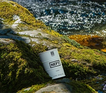 A NEFT Vodka white barrel laying gently on mossy rocks along a stream of water.