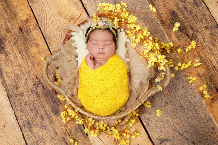 A newborn baby swaddled in bright yellow fabric, sleeping peacefully in a rustic basket.