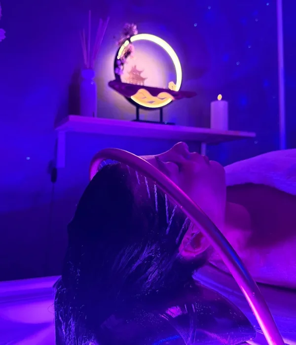 A smiling young man with crossed arms, wearing a plaid shirt and white t-shirt, poses against a dark background.