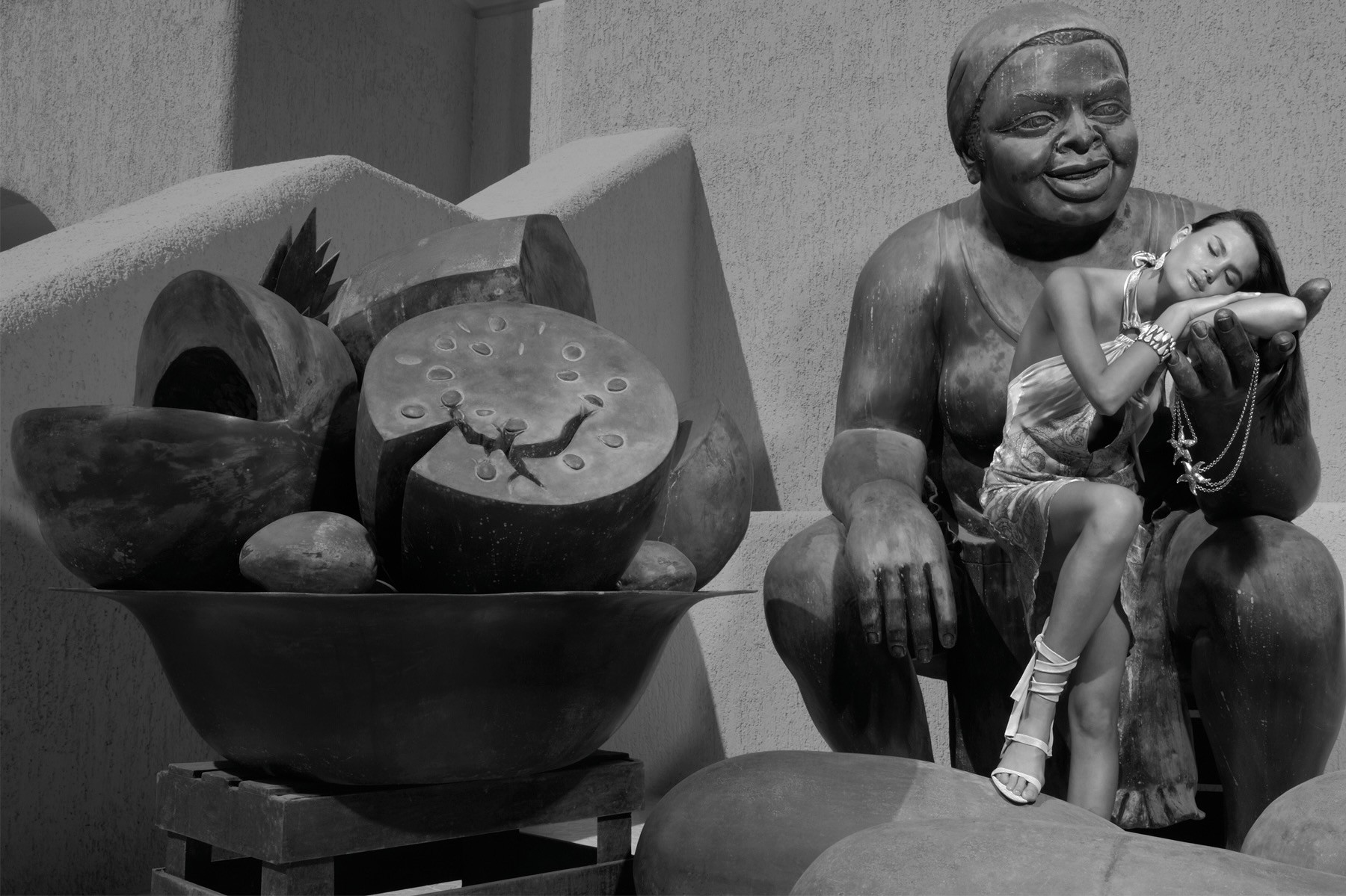 Black-and-white fashion portrait seated beside a sculpture
