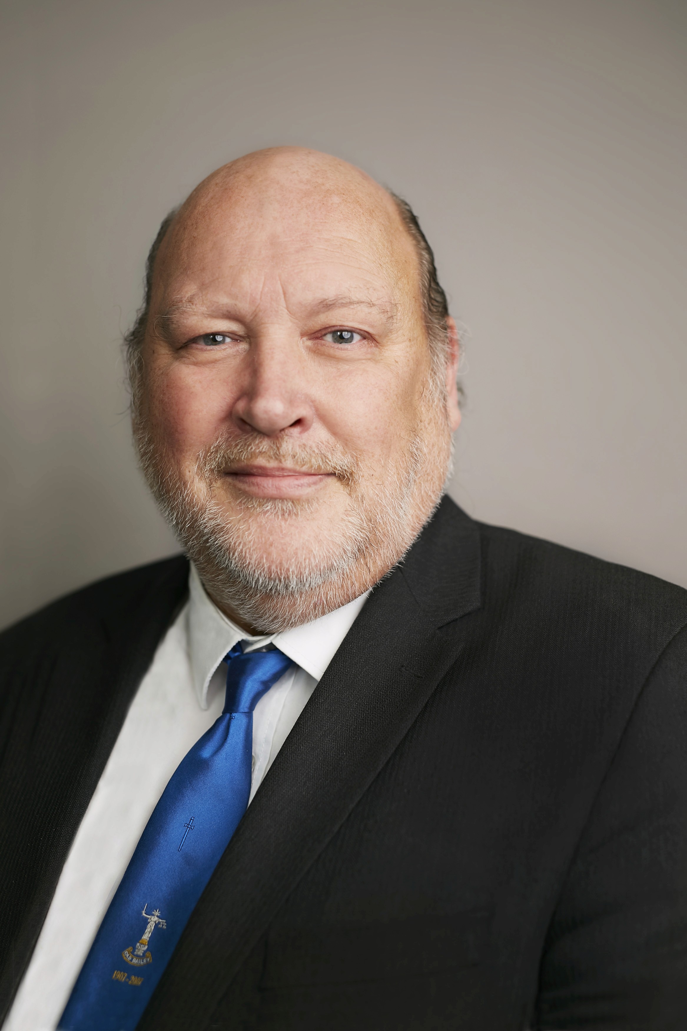 Man in a suit and blue tie with a badge.