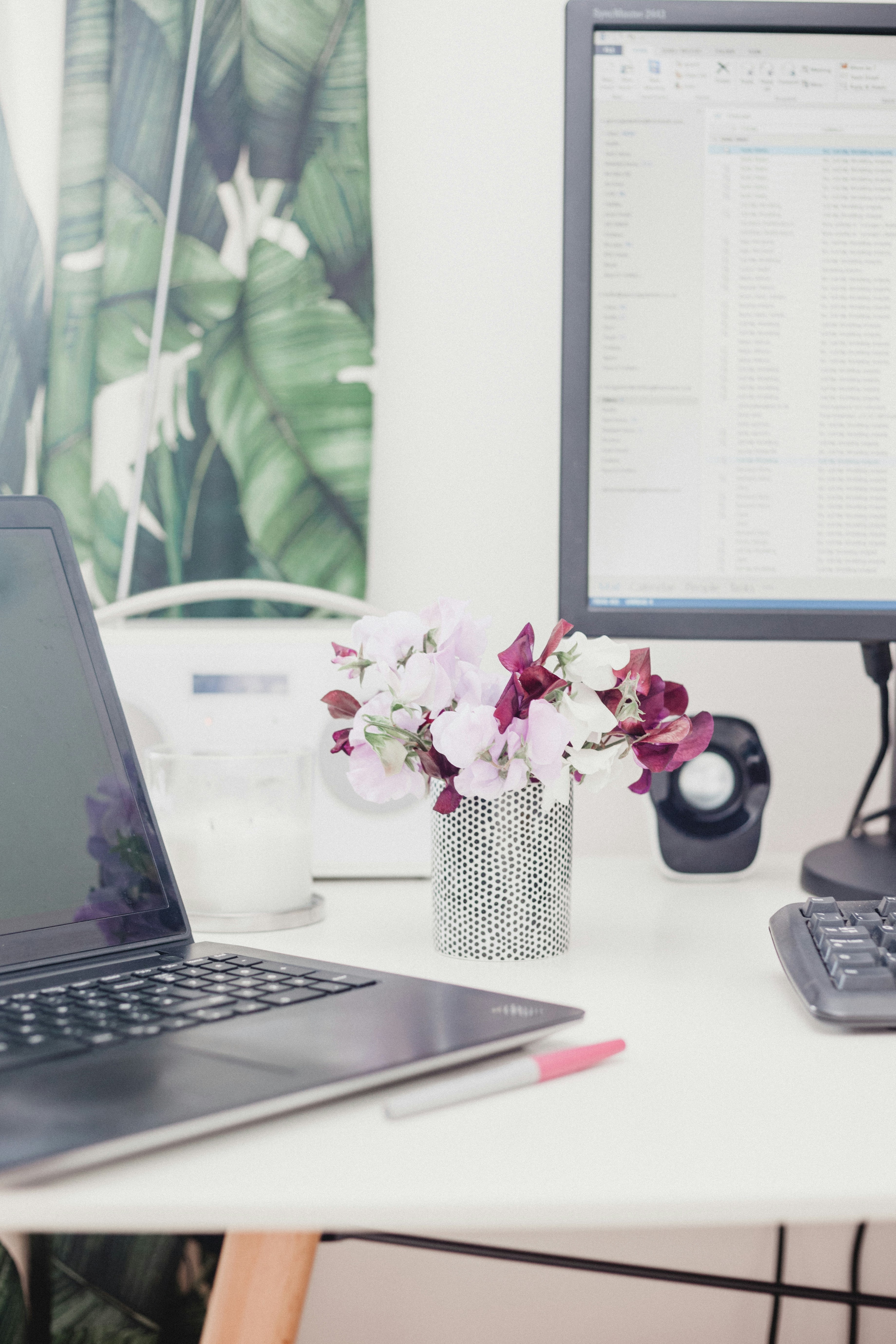 Partially visible desk with a small flower, partially visible laptop and monitor.