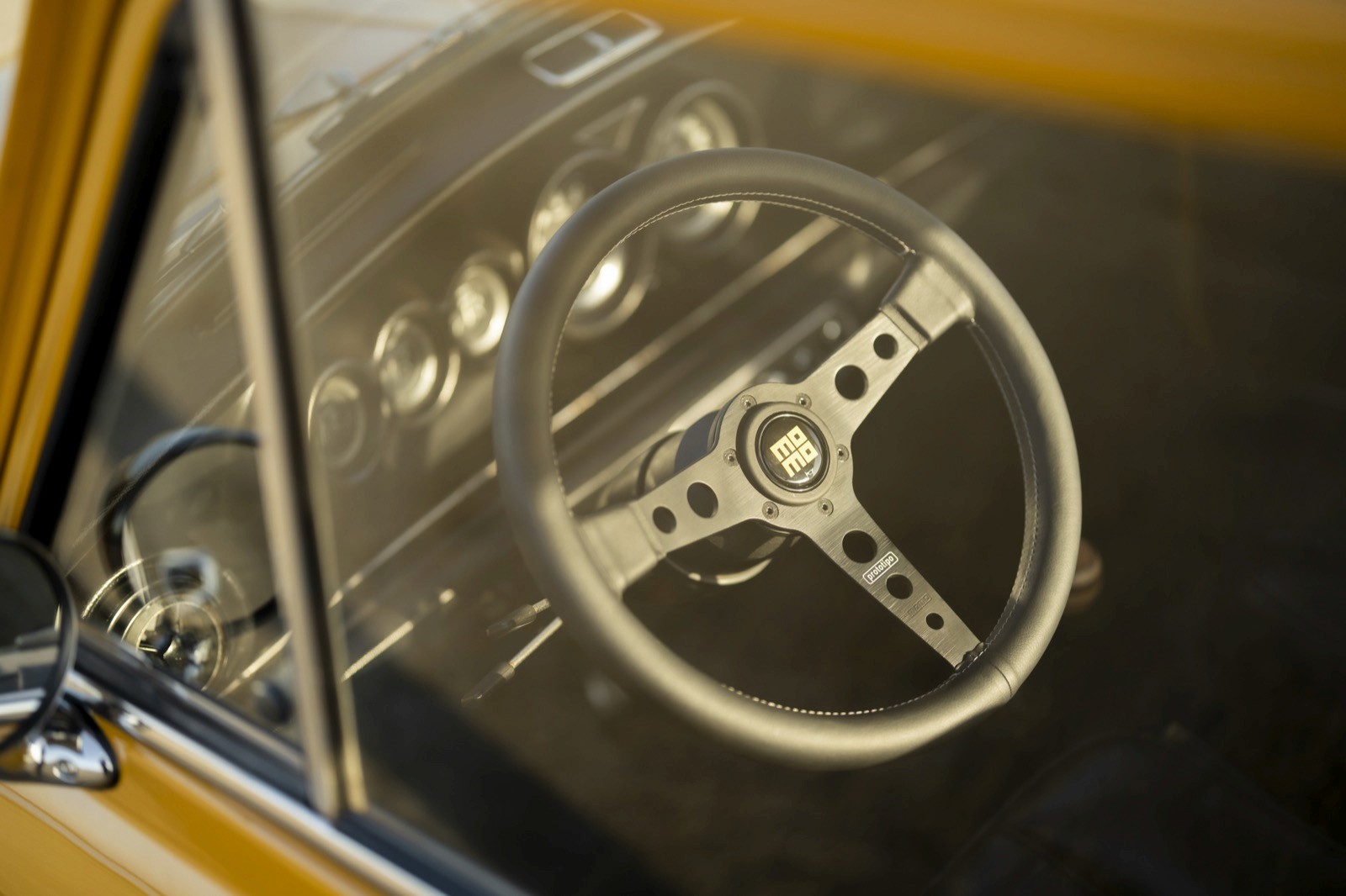 Close-up of a car's dashboard showing a steering wheel and various vintage gauges, illuminated by sunlight.