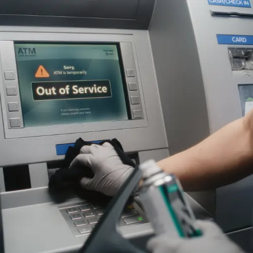 Professional bank cleaning technician disinfecting ATM keypad with EPA-approved cleaning solution