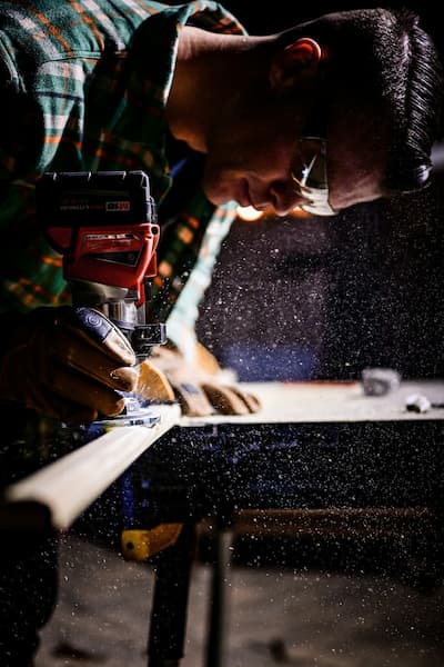 Carpenter Using power tool to shape wood while wearing safety goggles and gloves in workshop.