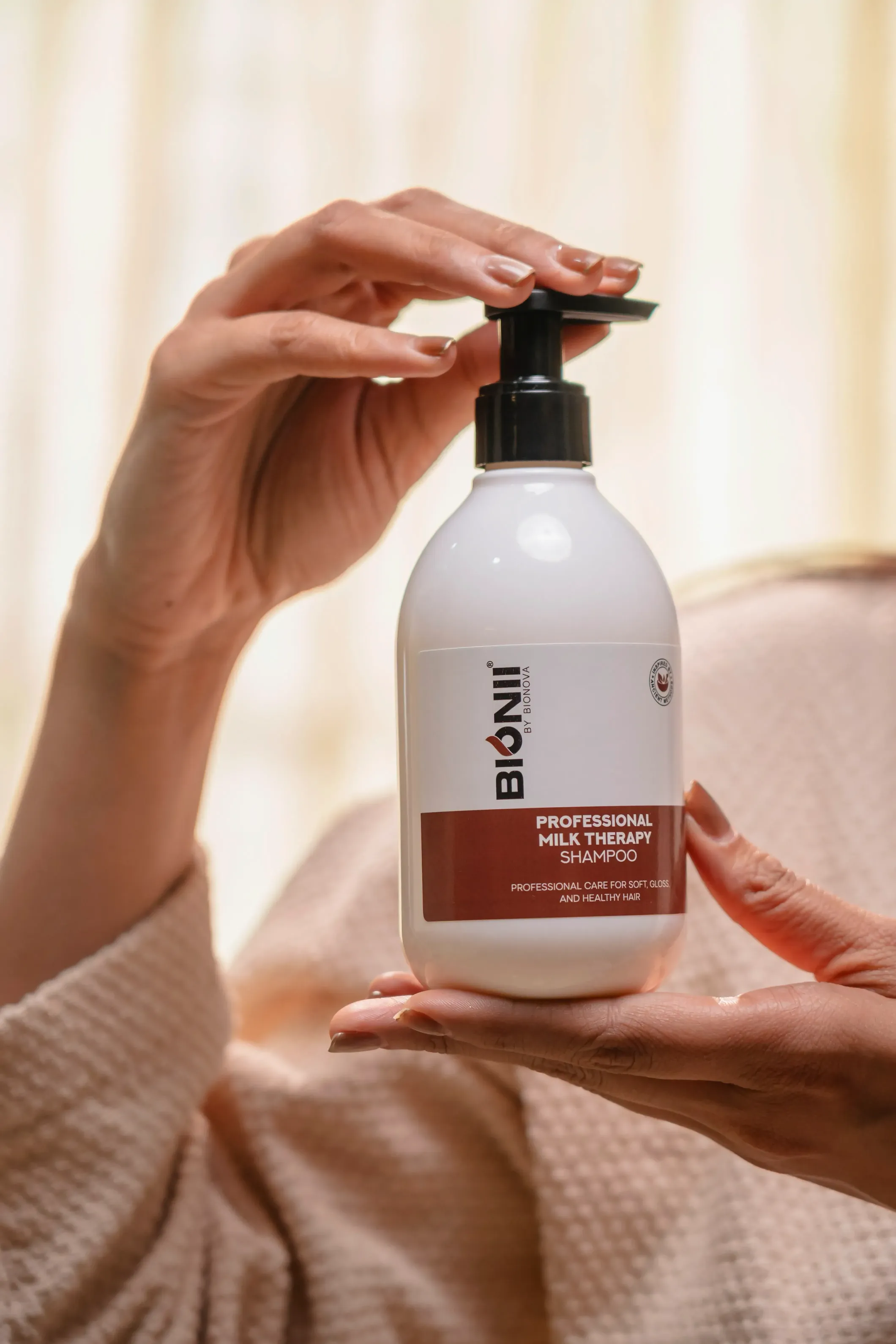 A hand holding a bottle of lotion with a pump top, set against a soft, light background.