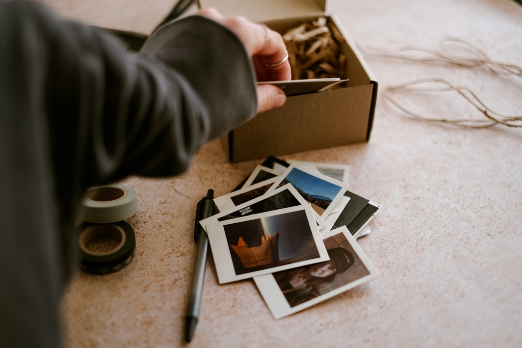 A person organizes a collection of printed photos on a table, alongside rolls of tape and a pen, evoking a sense of nostalgia and the joy of preserving memories.